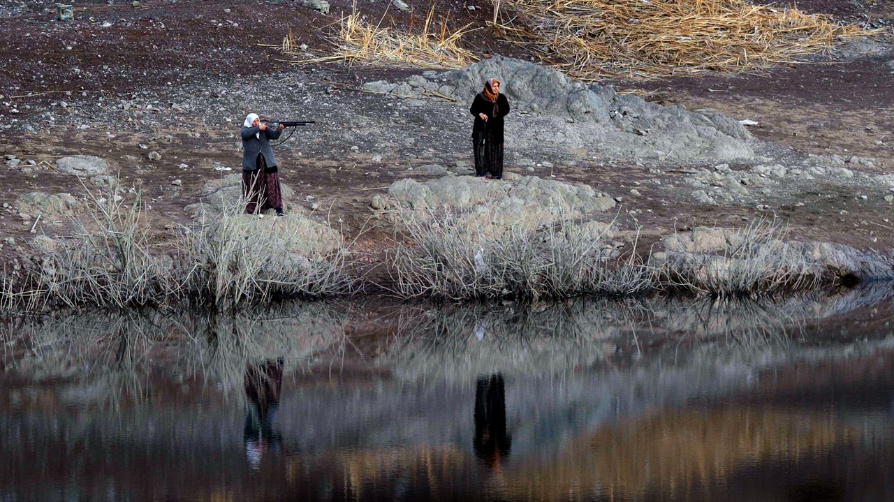 A woman in a headscarf aiming a rifle